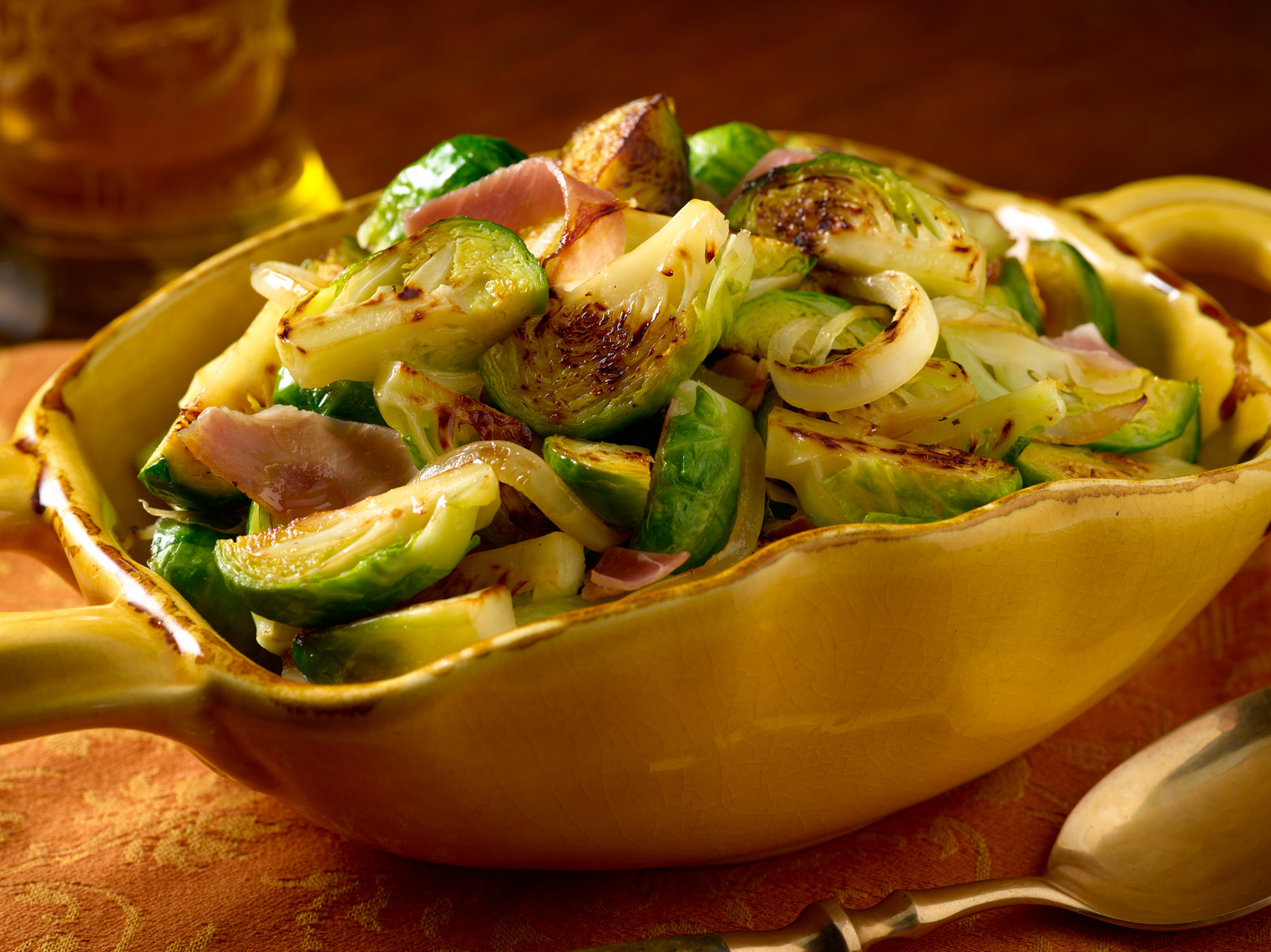 Roasted Brussel sprouts in yellow serving dish on orange tablecloth Fantich studio food photography.