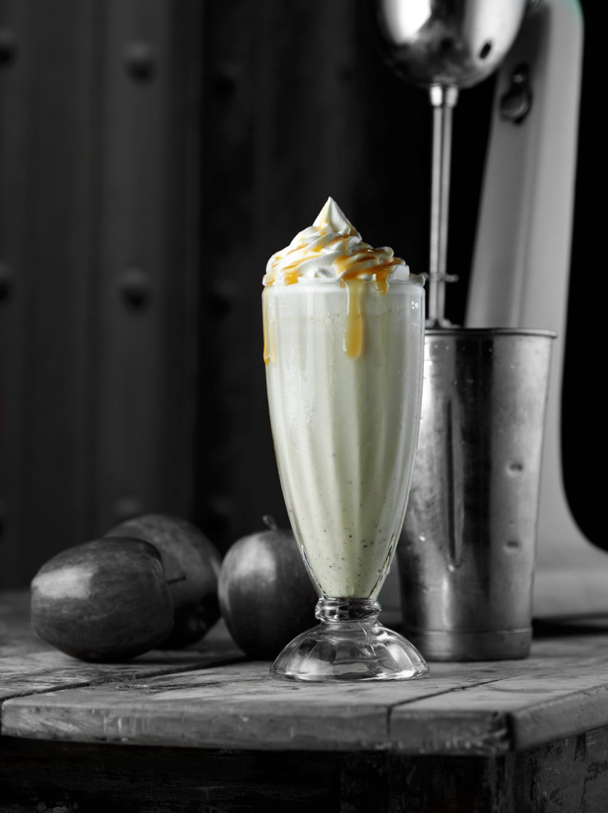 Carmel apple milk shake with whip cream and Carmel sauce on rustic wood table with apples and Hamilton beach blender Fantich studio food photography