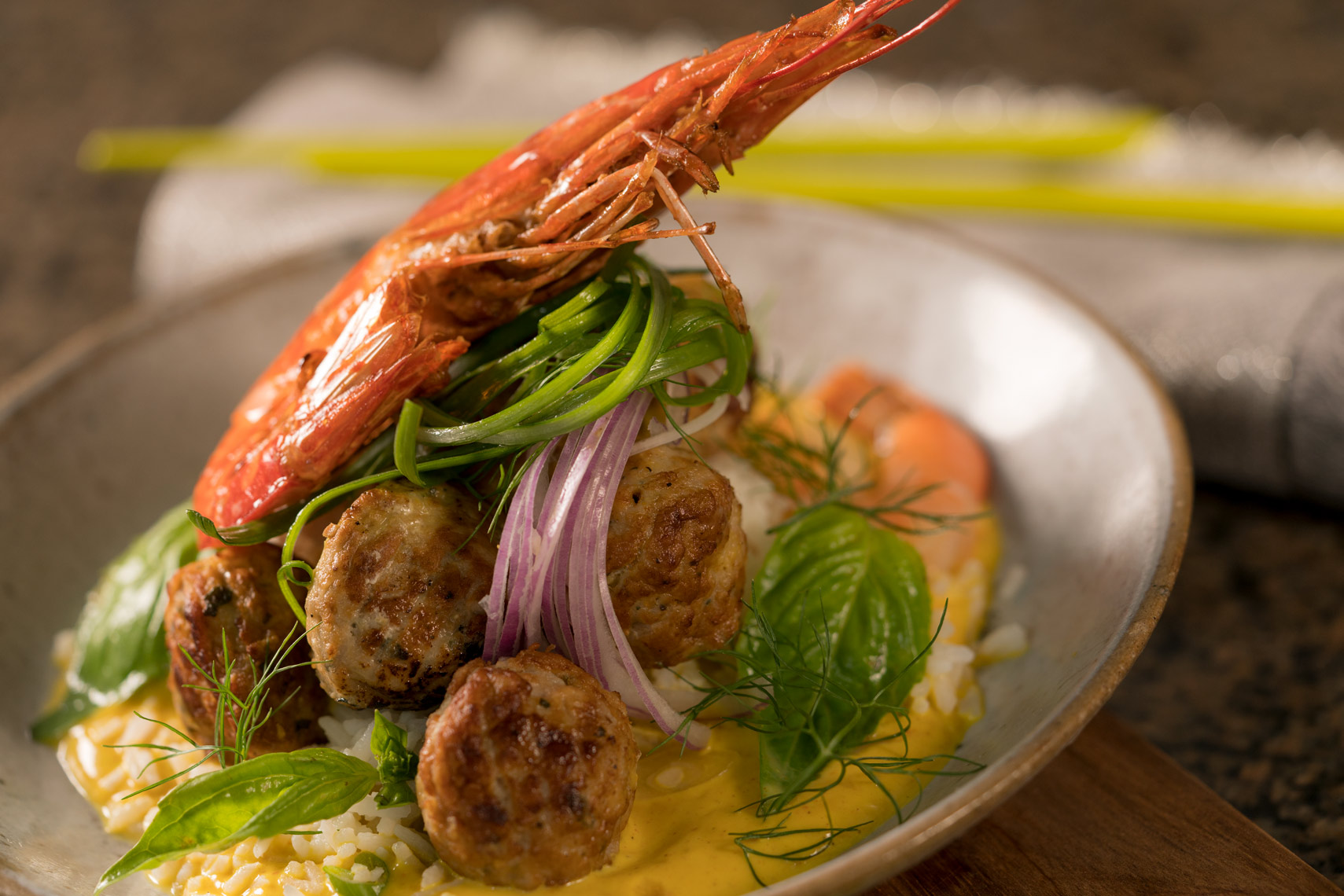 Meatballs and whole prawns with rice garnished with onions and basil in a rustic bowl  on wood en surface Fantich studio food photography.