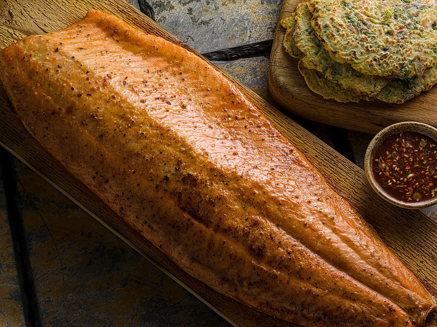 Siraracha maple glazed whole salmon filet on cedar plank on slate tiles with potatoes pancakes on wooden serving  board Fantich studio food photography